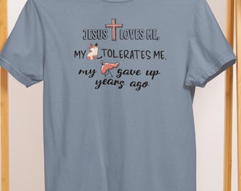 May include: A light blue t-shirt with the text "Jesus Loves Me, My Tolerates Me, My Gave Up Years Ago" and a cross graphic. The shirt also features a cartoon fox and a piece of meat.