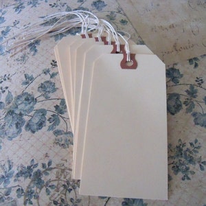 May include: A set of six blank, off-white gift tags with brown string attached. The tags are on a floral patterned background.