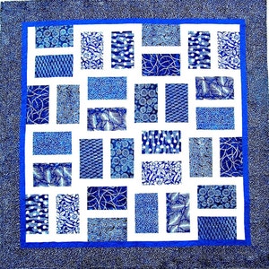 Könnte beinhalten: Eine blaue und weiße Patchwork-Decke mit weißem Hintergrund und blauem Rand. Die Decke besteht aus verschiedenen blauen und weißen Stoffen mit verschiedenen Mustern.