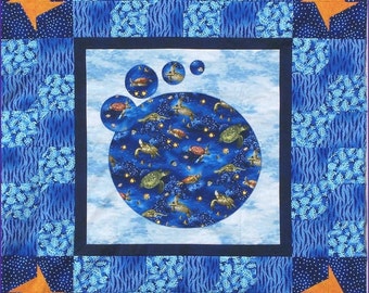 May include: A blue and orange patchwork quilt with a large circle in the center. The circle is filled with a pattern of sea turtles and jellyfish on a blue background. The quilt is surrounded by a blue border.