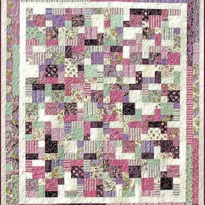 Könnte beinhalten: Eine Quiltdecke mit Patchwork-Muster, die aus Quadraten mit verschiedenen floralen und geometrischen Mustern in den Farben Rosa, Lila, Grün und Weiß besteht.