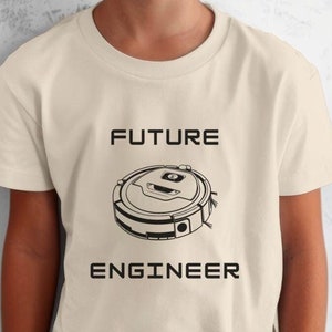 May include: A young person wearing a cream colored t-shirt with the text "FUTURE ENGINEER" and a black and white illustration of a robot vacuum cleaner.