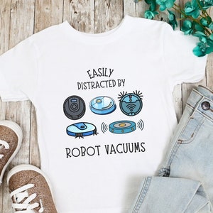 Puede incluir: Camiseta blanca con el texto "Fácilmente distraído por los robots aspiradores" y un gráfico de cinco robots aspiradores diferentes.