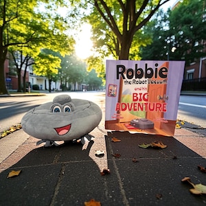 May include: A plush, gray robot vacuum toy with a smiling face and blue eyes sits next to a children's book titled "Robbie the Robot Vacuum and his BIG Adventure." The book cover features a cartoon illustration of a robot vacuum.
