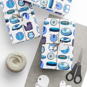 May include: White wrapping paper with a repeating pattern of blue robot vacuum cleaners. The paper is rolled up and tied with twine. There are also some white circles on the table.