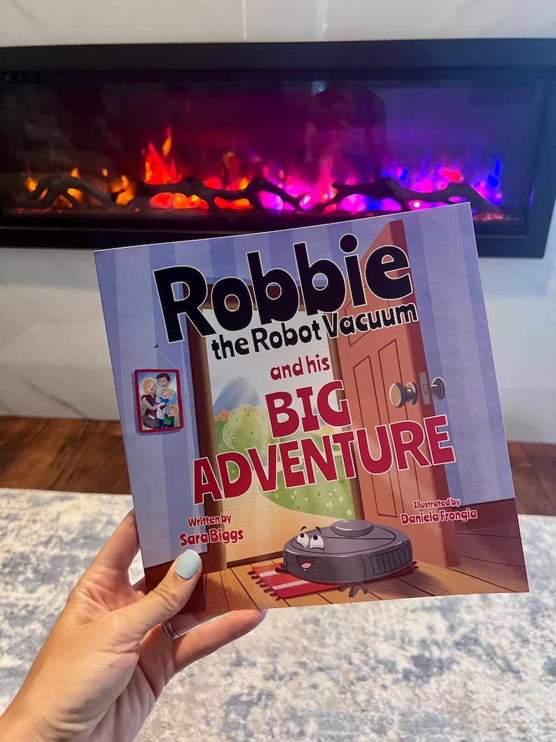May include: A children's book titled "Robbie the Robot Vacuum and his Big Adventure." The cover features a cartoon robot vacuum, a red welcome mat, and the text "BIG ADVENTURE" in large letters. The book is written by Sara Biggs and illustrated by Daniela Frongia.