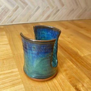 Peut inclure: Un porte-serviettes en papier en céramique fait à la main avec un glaçage bleu et vert. Le porte-serviettes a un design unique avec une découpe pour le rouleau de papier absorbant.