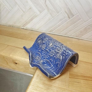 May include: A blue ceramic dish with a white floral design. The dish is shaped like a wave and has a raised edge.