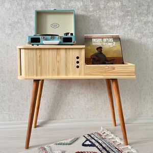 May include: A light blue record player with a wooden stand and a record on the shelf. The record is by Neset Ertaş and is titled "Olmsuz T&uuml;rk&uuml;ler 2".