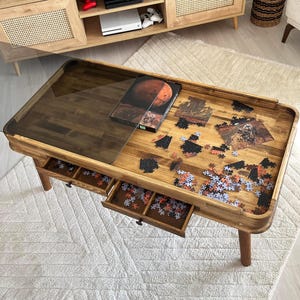 May include: A wooden coffee table with a glass top and two drawers. The table has a puzzle on top of it and a book with a picture of Mars on the cover. The table is sitting on a white rug.