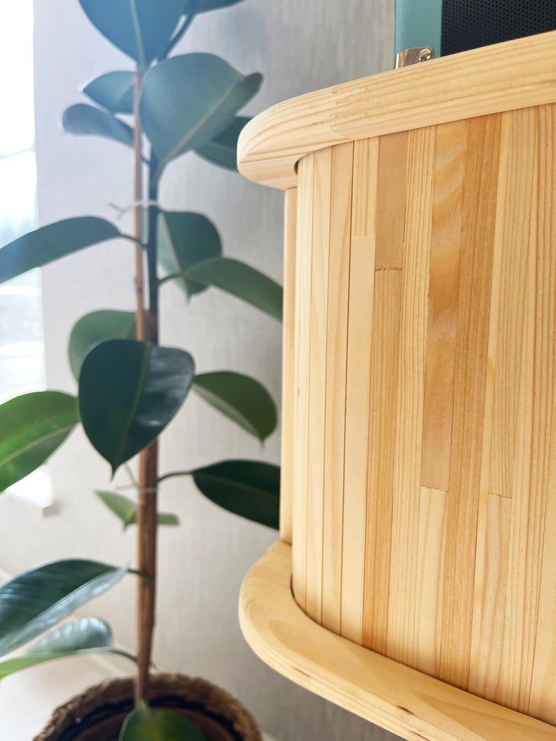 May include: Close-up of a light wood cabinet with a curved edge and vertical slats. The cabinet is made of natural wood with a light brown finish.