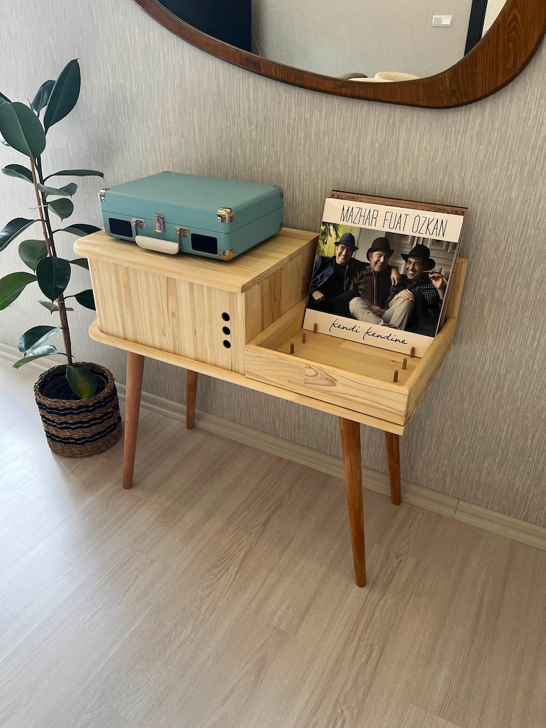 May include: A light blue record player sits on a wooden record stand with a record album titled "Mazhar Fuat Ozkan kendi kendine" on the right side of the stand.