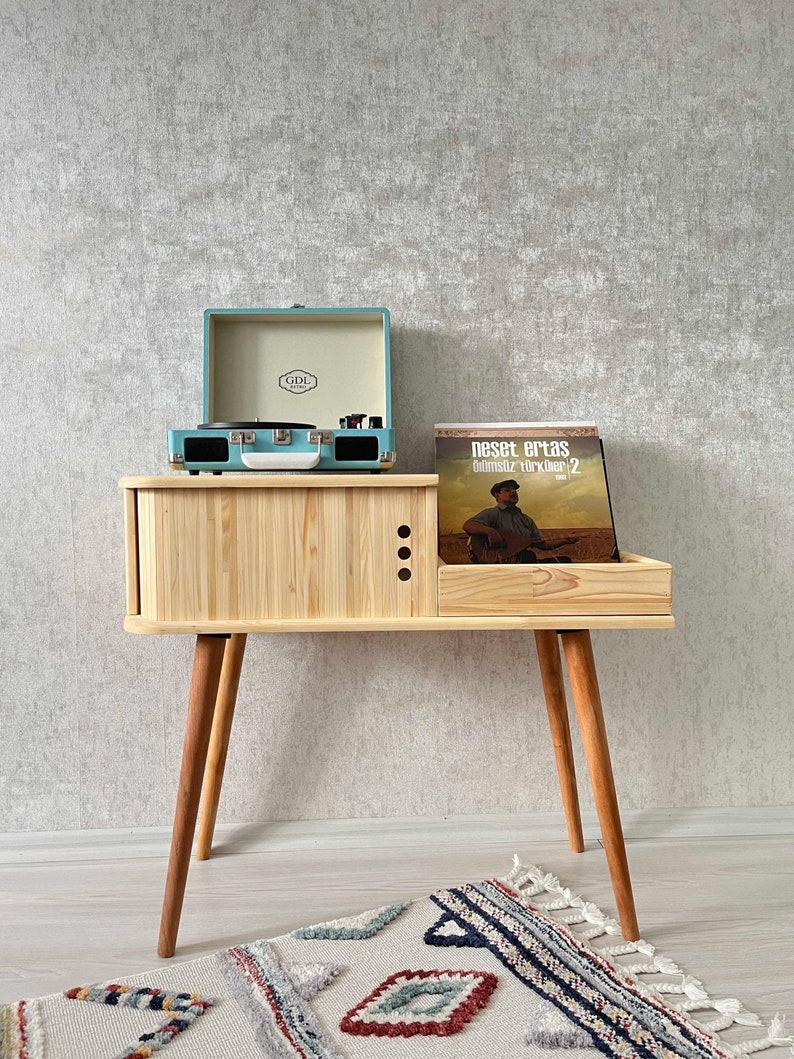 May include: A light blue record player with a wooden stand and a record on the shelf. The record is by Neset Ertaş and is titled "Olmsuz T&uuml;rk&uuml;ler 2".
