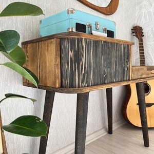 May include: A wooden console table with black stained legs and a light blue vintage record player on top. The table has a rustic, reclaimed wood look and is perfect for a living room or bedroom.