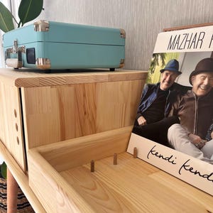 May include: A light wood record player stand with a light blue record player on top and a vinyl record with a photo of two men on the bottom shelf. The record is titled "Mazhar "kendi kendi"