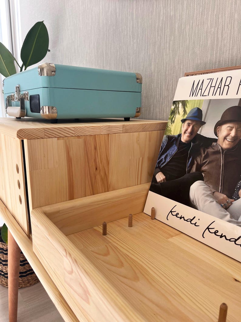 May include: A light wood record player stand with a light blue record player on top and a vinyl record with a photo of two men on the bottom shelf. The record is titled "Mazhar "kendi kendi"