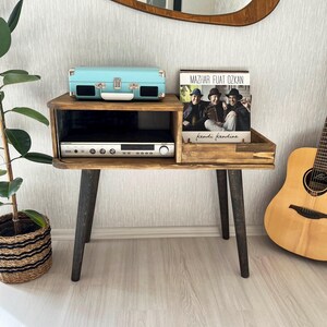 May include: A wooden record player stand with black legs. A vintage record player, a record album, and a guitar are on the stand. The album is titled "Mazhar Fuat Ozkan - Kendi Kendine".