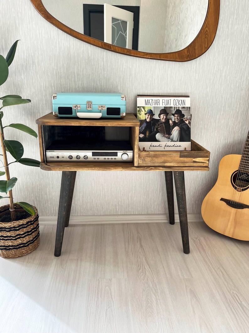 May include: A wooden record player stand with black legs. A vintage record player, a record album, and a guitar are on the stand. The album is titled "Mazhar Fuat Ozkan - Kendi Kendine".