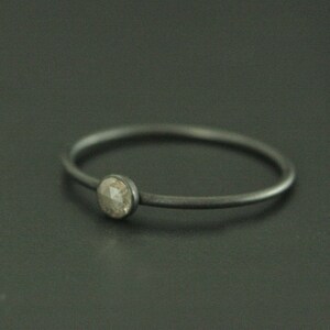May include: A simple silver ring with a single, round, grey diamond.