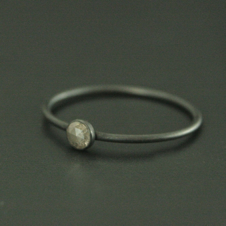 May include: A simple silver ring with a single, round, grey diamond.