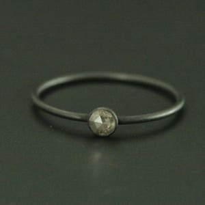 May include: A simple silver band ring with a single, round, grey diamond.