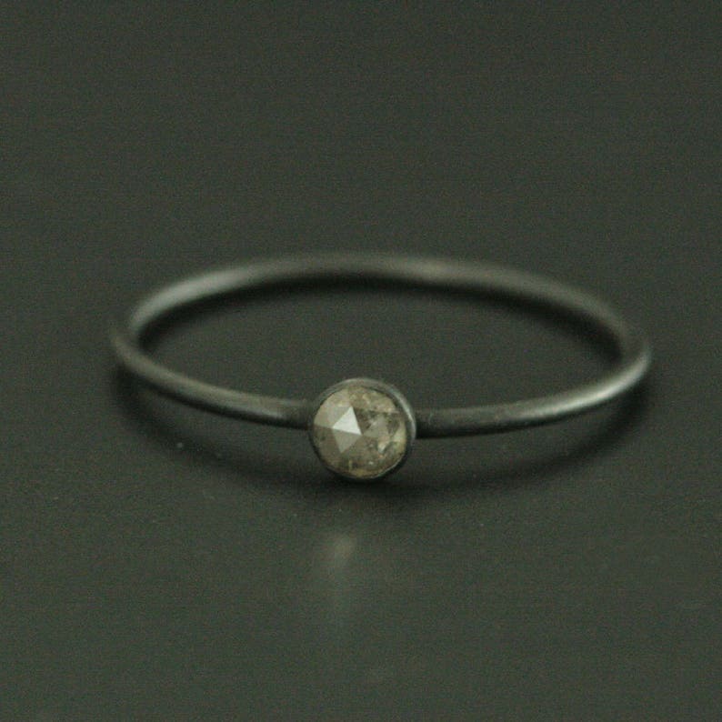 May include: A simple silver band ring with a single, round, grey diamond.