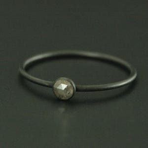 May include: A simple black band ring with a single, round, gray gemstone set in the center.
