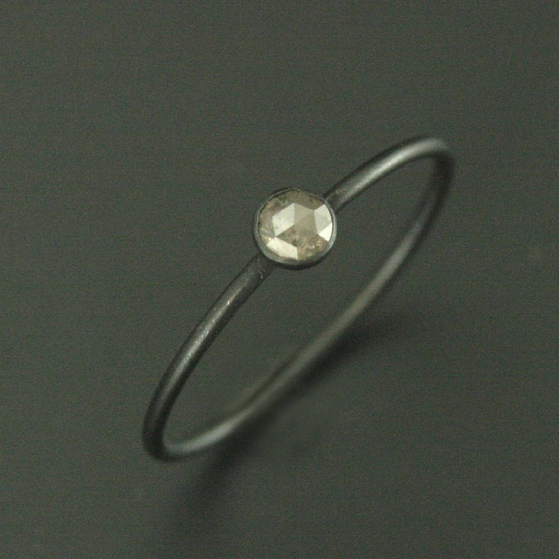 May include: A simple silver band ring with a single, round, faceted, grey diamond.