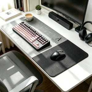 May include: A large rectangular desk mat featuring a two-tone design with a light grey textured surface on the left and a solid black surface on the right. The mat displays the black text "ALEX STUDIO" with a logo above it on the grey section.