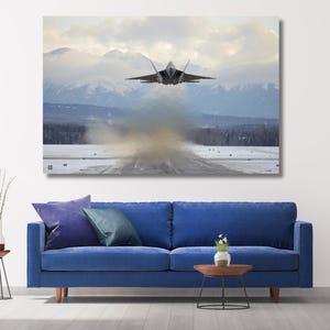 Op de afbeelding: Een canvas print van een straaljager die opstijgt vanaf een besneeuwde landingsbaan, met bergen op de achtergrond. De jet is van achteren te zien, met een spoor van rook en damp.