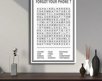 May include: A framed word search puzzle with the text "FORGOT YOUR PHONE?" and a list of bathroom-related words. The puzzle is black and white, with a black frame. The image is displayed on a dark wooden surface.