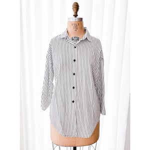 Op de afbeelding: Een wit en zwart gestreept overhemd met knopen en een kraag. Het overhemd heeft lange mouwen en een losse pasvorm.