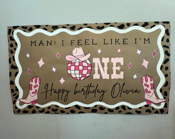 Puede incluir: Bandera de cumpleaños con fondo marrón y borde de estampado de leopardo. La bandera presenta un sombrero de vaquero rosa, una bola de discoteca y las palabras "ONE" y "Happy birthday Olivia". Estrellas rosas y botas de vaquero completan el diseño.