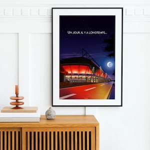 May include: A black framed poster with a nighttime illustration of a stadium with red lights and a crescent moon in the sky. The text "UN JOUR, IL Y A LONGTEMPS..." is at the top of the poster.