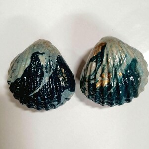 May include: Two seashells painted in a blue and gold marbled design. The shells are a light blue color with dark blue and gold accents.