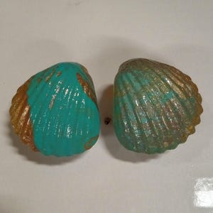 Könnte beinhalten: Ein Paar türkisfarbene und goldene Muschelohrringe. Die Muscheln sind mit einem türkisfarbenen Überzug bemalt und haben goldene Akzente.