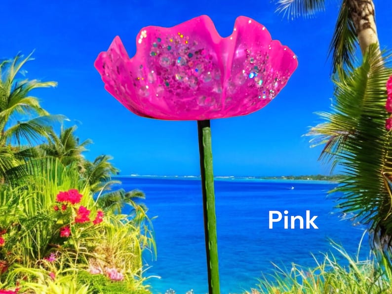 Pu&ograve; includere: Un fiore di vetro rosa con dettagli glitterati, su uno sfondo di spiaggia tropicale. Il fiore &egrave; su uno stelo di metallo verde. Il testo "Pink" &egrave; visibile nell'angolo in basso a destra dell'immagine.