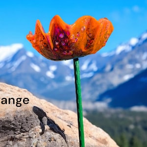 Pu&ograve; includere: Fiore di papavero di vetro arancione con stelo verde, sullo sfondo di montagne innevate.
