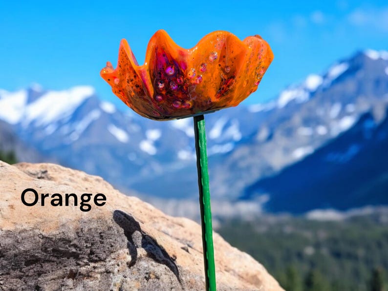 Pu&ograve; includere: Fiore di papavero di vetro arancione con stelo verde, sullo sfondo di montagne innevate.