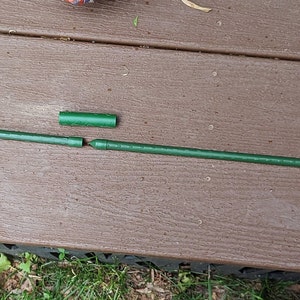 Pu&ograve; includere: Un'asta di metallo verde &egrave; rotta in tre pezzi. L'asta &egrave; appoggiata su una superficie di legno marrone. Un oggetto decorativo rotondo, arancione e giallo si trova sul lato destro dell'immagine.