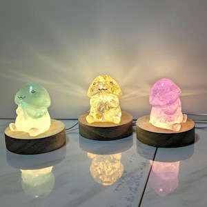 May include: Three small crystal lamps shaped like animals, each with a different color. The lamps are on wooden bases and emit a warm glow.