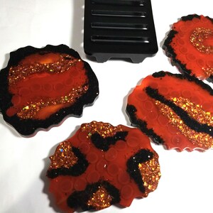 May include: Set of four red and black agate-style coasters with gold glitter accents. The coasters have an irregular, organic shape.
