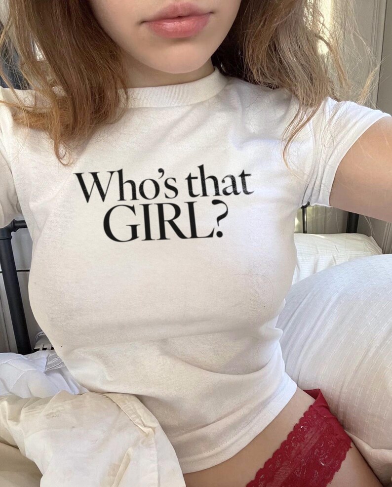 Może przedstawiać: Biały crop top z kr&oacute;tkimi rękawami i nadrukiem "Who's that GIRL?" w kolorze czarnym.