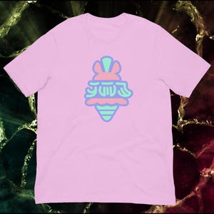 May include: A light pink t-shirt featuring a colorful graphic. The graphic is a stylized ice cream cone with a bunny-like design and Japanese text. The design uses shades of pink, blue, and green.