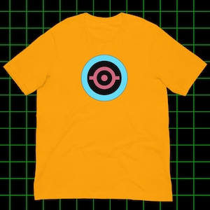 Puede incluir: Camiseta de color amarillo mostaza con un diseño gráfico circular. El diseño gráfico tiene un anillo exterior azul claro, un anillo interior negro y un centro rosa con un diseño estilizado. La camiseta es de material suave.
