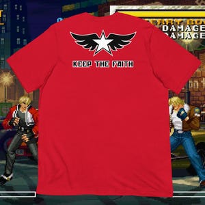 May include: A red t-shirt featuring a black and white star with wings design and the text "KEEP THE FAITH". The shirt is displayed against a pixelated background with fighting game characters.