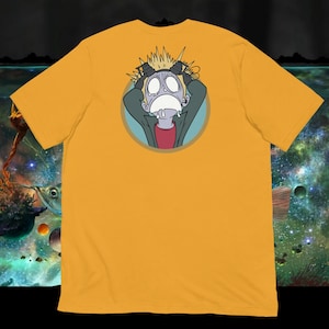 Peut inclure: T-shirt jaune moutarde avec une illustration de dessin animé d'une personne à l'expression choquée, les mains sur la tête. Le graphisme est dans un design circulaire avec un contour bleu. La personne porte une veste verte et une chemise rouge.