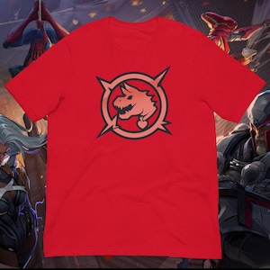 Puede incluir: Camiseta roja con un diseño circular que presenta una cabeza de dragón estilizada en tonos rosa y negro. El dragón tiene una etiqueta en forma de corazón. El diseño está rodeado por un círculo negro y cuatro líneas puntiagudas.