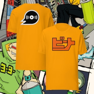 Op de afbeelding: Twee oranje t-shirts met grafische ontwerpen. Eén shirt heeft een zwart-wit vinylplaatontwerp in een tekstballon. Het andere shirt toont Japanse karakters in oranje en zwart. De shirts hebben korte mouwen.