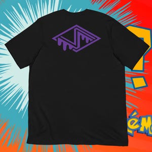 Può includere: T-shirt nero con un design geometrico viola sul retro. Il design ha la forma di un diamante con una lettera "N" stilizzata e dettagli a goccia. La maglietta è realizzata in un materiale morbido.